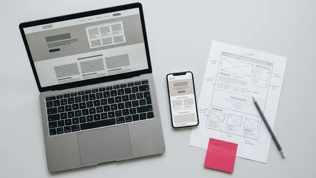 A laptop showing a landing page next to a phone with the mobile version and a printed wireframe.