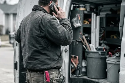 A tradesperson taking a call at the back of a work van.